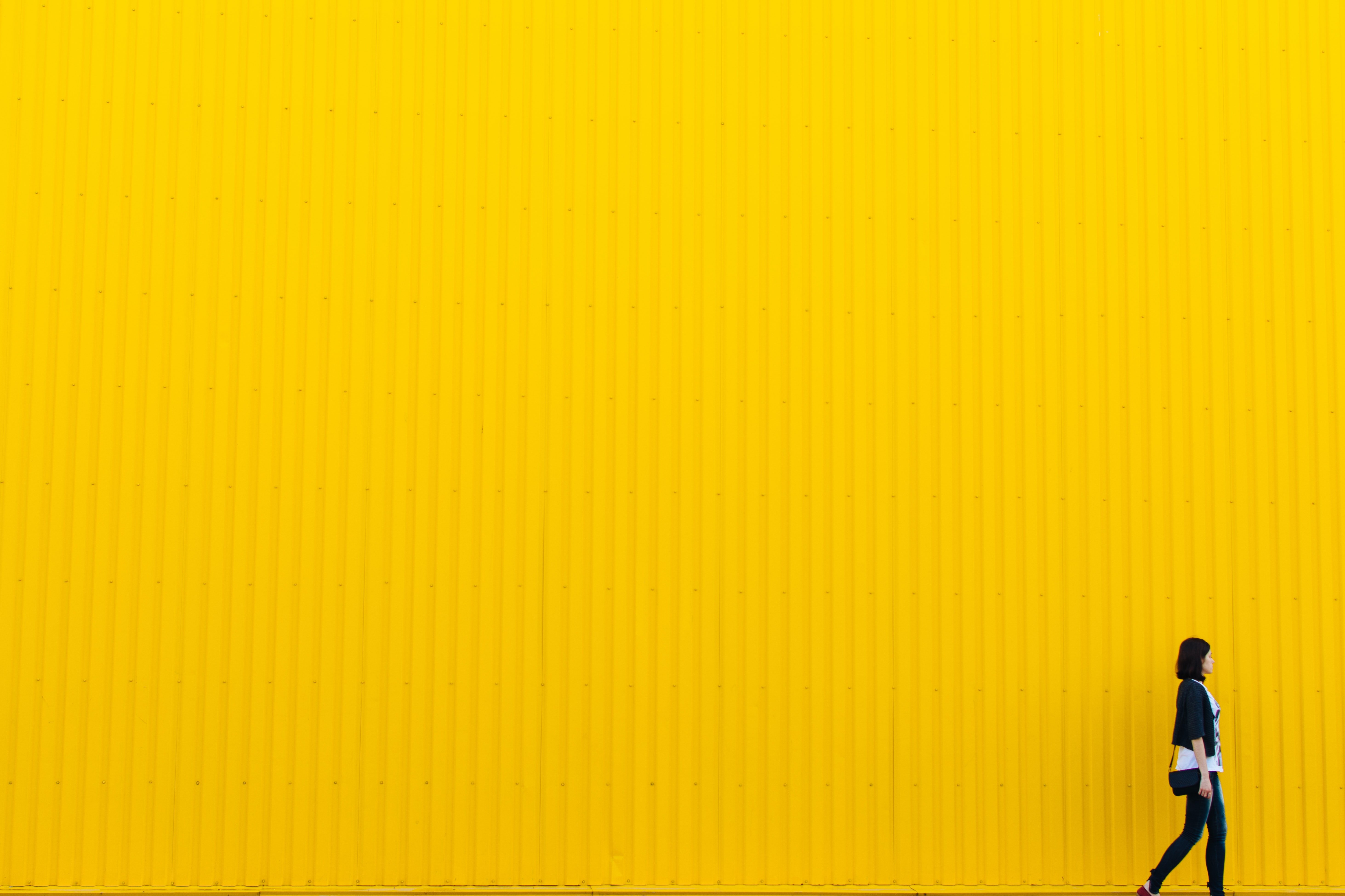woman walks in front of a bright yellow wall