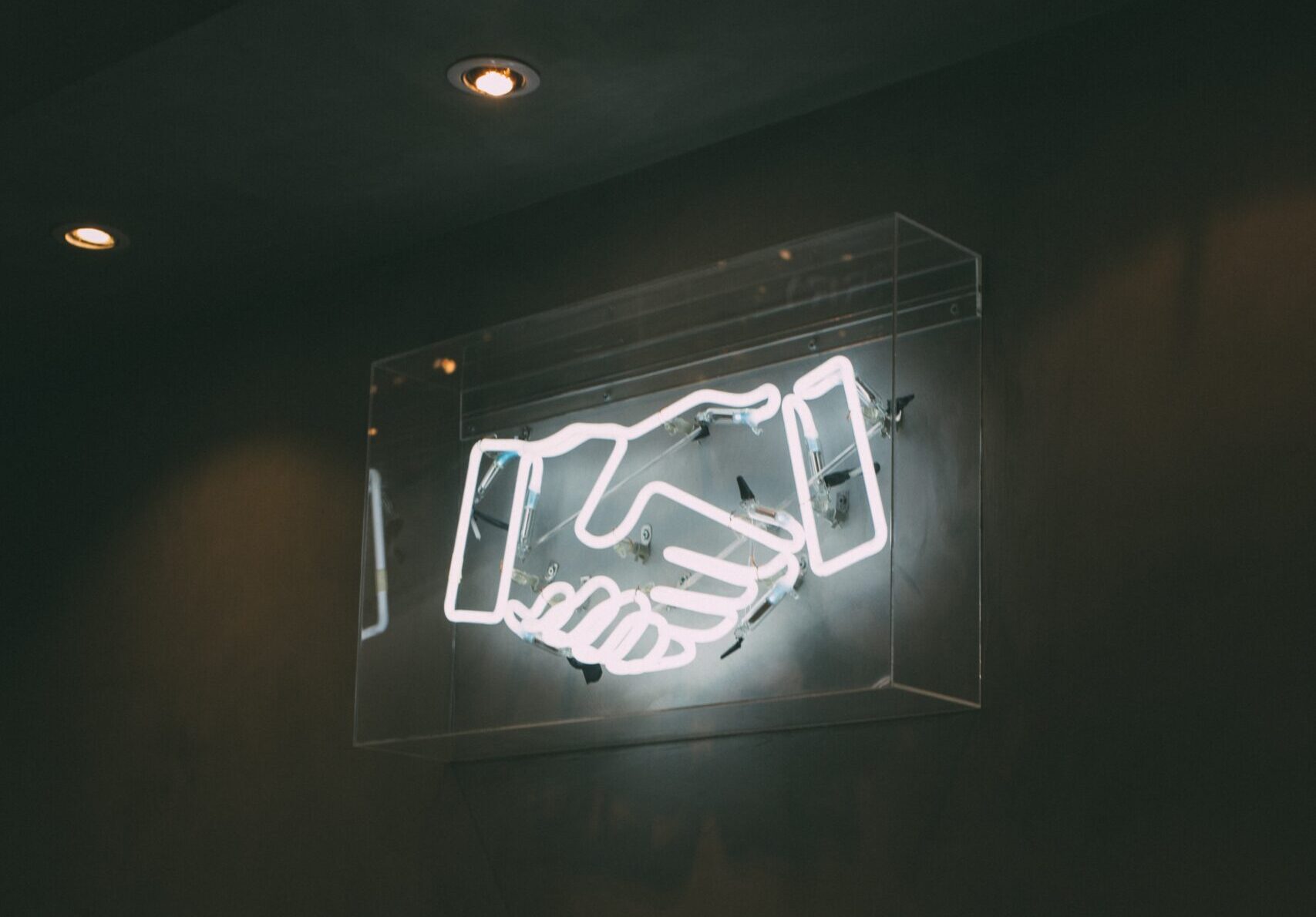 neon sign of a handshake against a black wall